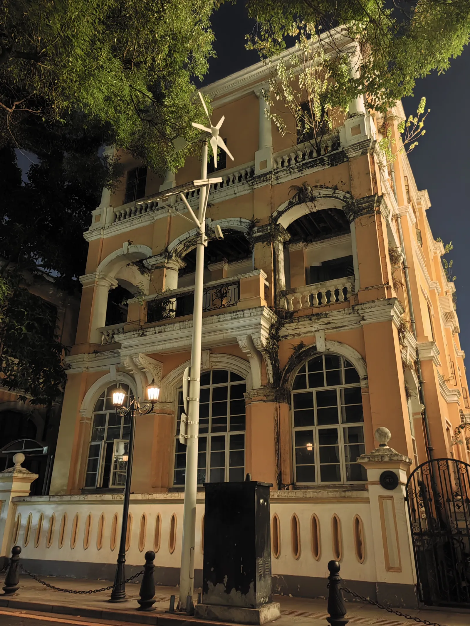 The same house at night, lit orange, with its pierced garden wall and arched ground-floor windows.